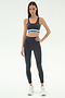 A woman wears SPLITS59's Ella High Waist Airweight 7/8 leggings in Graphite/Stone Blue with a matching sports bra, perfect for hot yoga, paired with white sneakers against a plain white background.