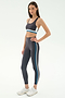 A woman stands in profile against a white background, wearing SPLITS59's Ella High Waist Airweight 7/8 leggings and matching sports bra in Graphite/Stone Blue—ideal for hot yoga sessions.