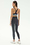 A woman faces away, wearing the SPLITS59 Ella High Waist Airweight 7/8 legging in Graphite/Stone Blue with a matching black sports bra and white sneakers—perfect for hot yoga—against a plain light background.