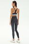 A woman faces away, wearing the SPLITS59 Ella High Waist Airweight 7/8 legging in Graphite/Stone Blue with a matching black sports bra and white sneakers—perfect for hot yoga—against a plain light background.