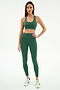A woman faces forward wearing the SPLITS59 Sara Airweight Bra in Arugula with matching high-waisted leggings and white sneakers, set against a plain white background.