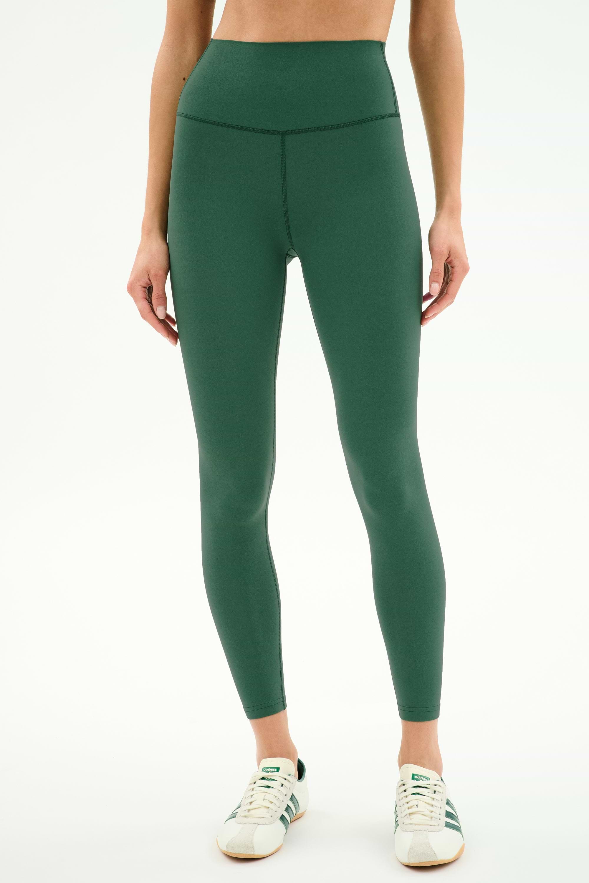 Model wears SPLITS59 Airweight High Waist Legging in Arugula with white sneakers, standing with arms relaxed at sides against a plain white background—ideal for hot yoga.