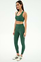 A woman stands against a plain background wearing the SPLITS59 Sara Airweight Bra in Arugula, matching leggings, and white Adidas sneakers with green stripes.