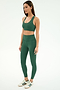 A woman stands against a plain background wearing the SPLITS59 Sara Airweight Bra in Arugula, matching leggings, and white Adidas sneakers with green stripes.
