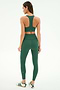 A woman stands with her back to the camera, wearing the SPLITS59 Sara Airweight Bra in Arugula and matching high-waisted leggings, made from a soft nylon-spandex blend, against a plain background.