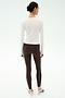 A woman stands with her back to the camera wearing SPLITS59’s Airweight Lite Long Sleeve Waist Length top in white, paired with striped brown leggings and white sneakers—ideal activewear for the gym on a plain light background.