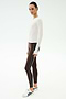 A woman wears the SPLITS59 Airweight Lite Long Sleeve Waist Length in white, paired with brown side-stripe leggings and white sneakers, standing against a plain light background.