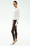A woman wears the SPLITS59 Airweight Lite Long Sleeve Waist Length in white, paired with brown side-stripe leggings and white sneakers, standing against a plain light background.