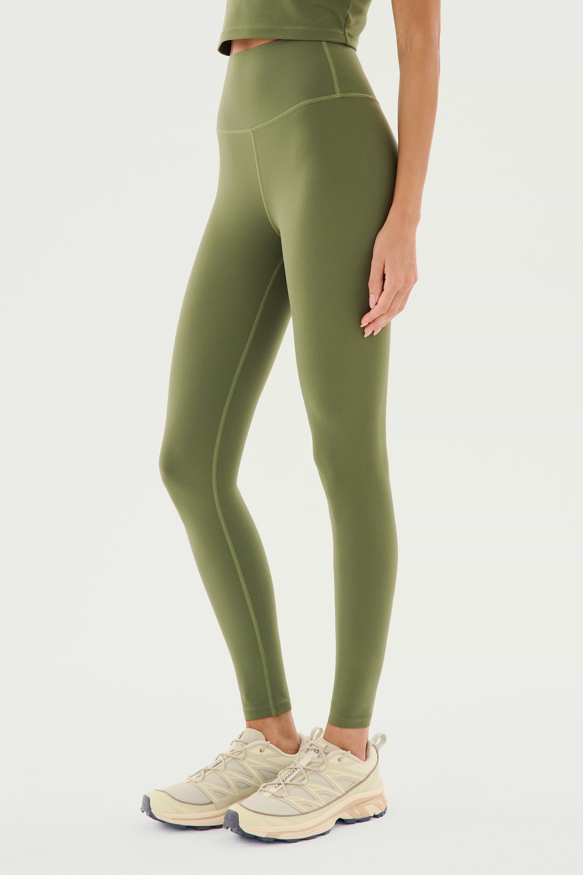 A person wearing the SPLITS59 Airweight High Waist Legging in Olive and beige sneakers is standing against a plain white background.