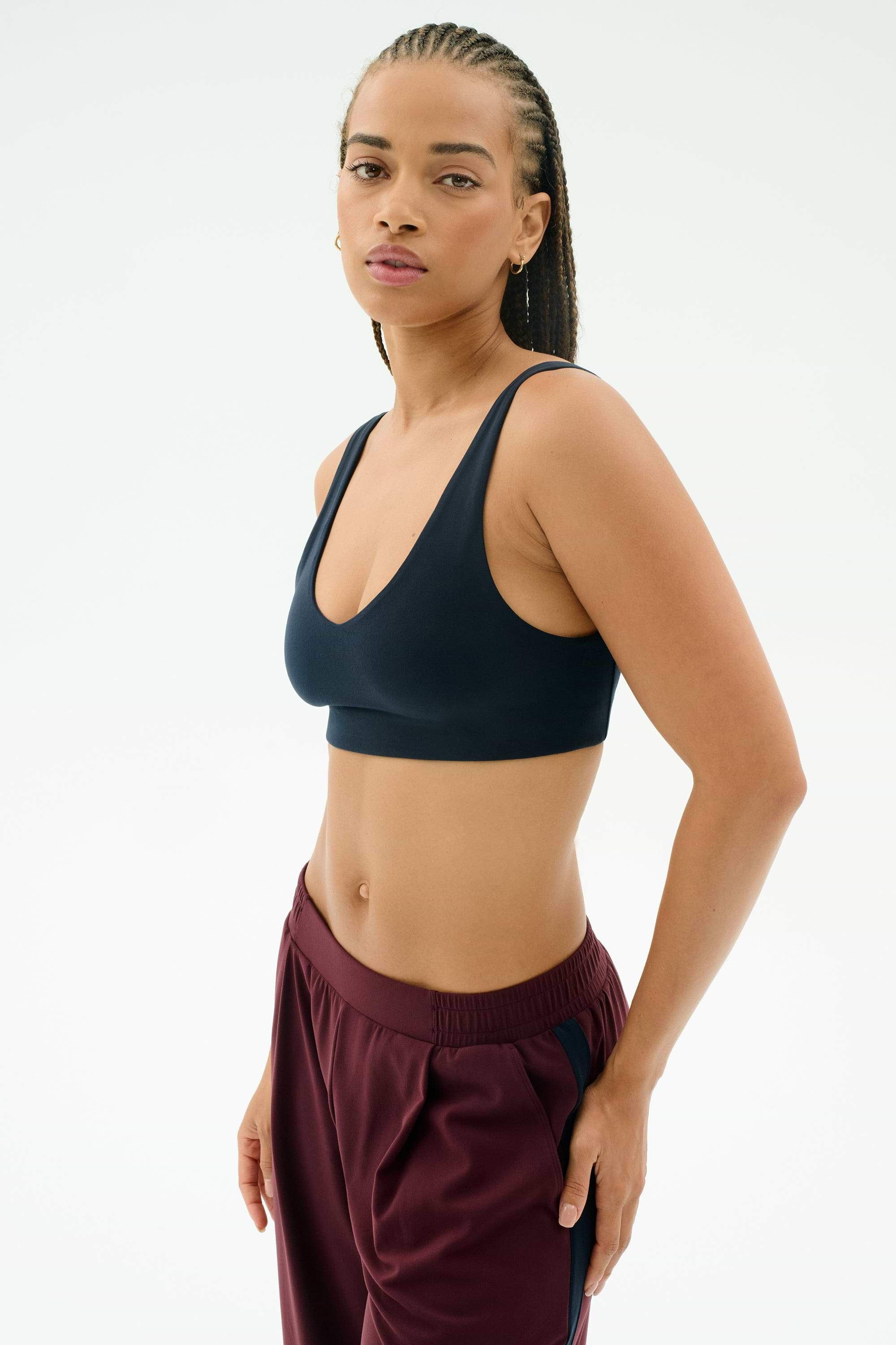 A woman wears the SPLITS59 Airweight Scoop Back Bra in Indigo, standing against a plain light background and looking at the camera.
