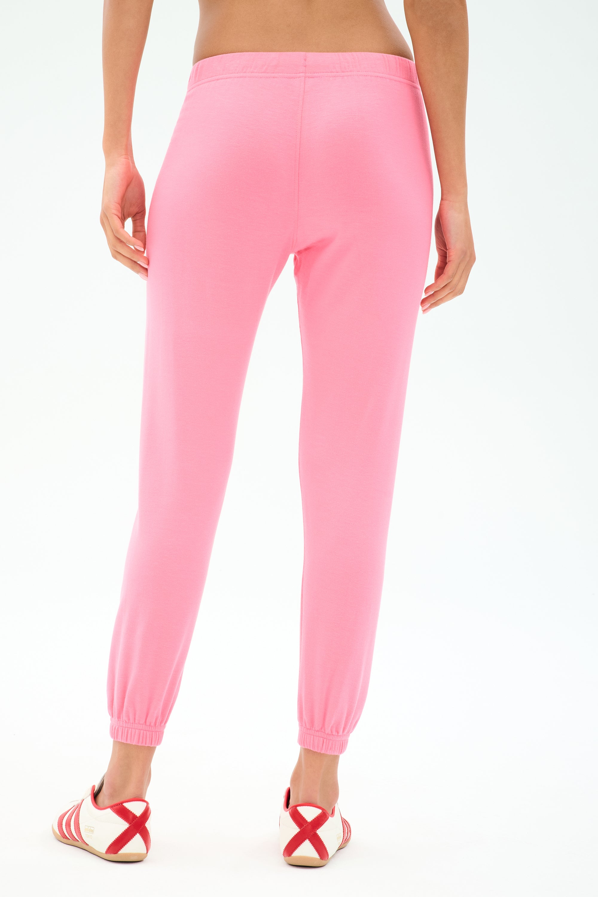 A person faces away wearing SPLITS59 Sonja Fleece Sweatpant in Strawberry and white sneakers with red accents, set against a plain white background.