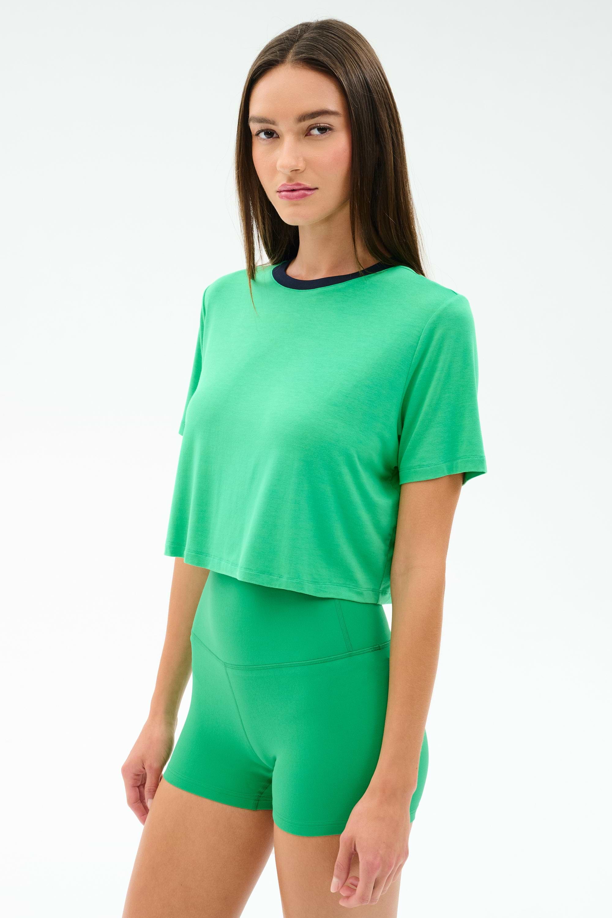 A woman stands against a white background wearing the SPLITS59 Djuna Crop Ringer in Spearmint/Indigo, a green cropped t-shirt made from soft viscose fabric.