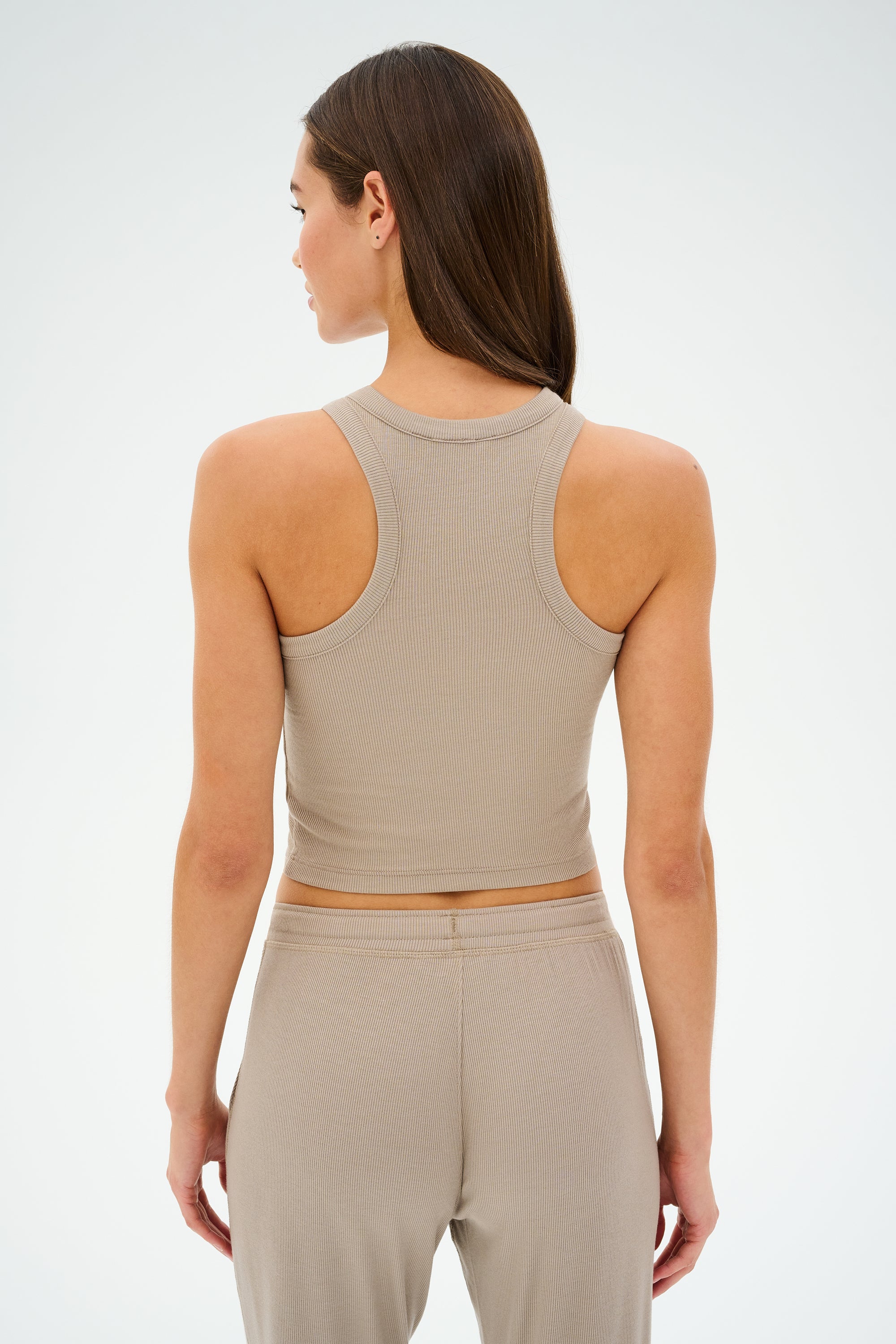 A woman with long hair wears the SPLITS59 Kiki Rib Crop Tank in Latte and pants, MADE IN LOS ANGELES, facing away from the camera against a plain background.
