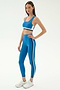 A woman wears the SPLITS59 Maci Airweight Bra in Stone Blue/Graphite, paired with matching leggings and white sneakers, standing against a plain white background.