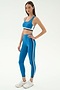 A woman wears the SPLITS59 Maci Airweight Bra in Stone Blue/Graphite, paired with matching leggings and white sneakers, standing against a plain white background.