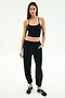 A woman stands against a white background wearing a black tank top, black SPLITS59 Nico Airweight Cargo Pant for lightweight comfort, and black sneakers with white stripes.