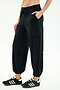 A person wears the SPLITS59 Nico Airweight Cargo Pant in black, paired with black sneakers with white stripes and a cropped black top, standing with one hand in a pocket for effortless comfort.