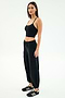 A woman poses against a plain background in the SPLITS59 Nico Airweight Cargo Pant in black, paired with a black crop top and black sneakers with white stripes.