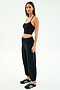 A woman poses against a plain background in the SPLITS59 Nico Airweight Cargo Pant in black, paired with a black crop top and black sneakers with white stripes.