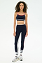 A woman faces forward in the SPLITS59 Eva Rigor Double Strap Bra in Indigo/White, styled for gym workouts with matching leggings and white sneakers, against a plain white background.