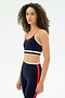A woman with curly hair wears the SPLITS59 Eva Rigor Double Strap Bra in Indigo/White with matching leggings, both featuring contrast color details, against a plain white background.