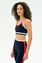 A woman with curly hair wears the SPLITS59 Eva Rigor Double Strap Bra in Indigo/White with matching leggings, both featuring contrast color details, against a plain white background.