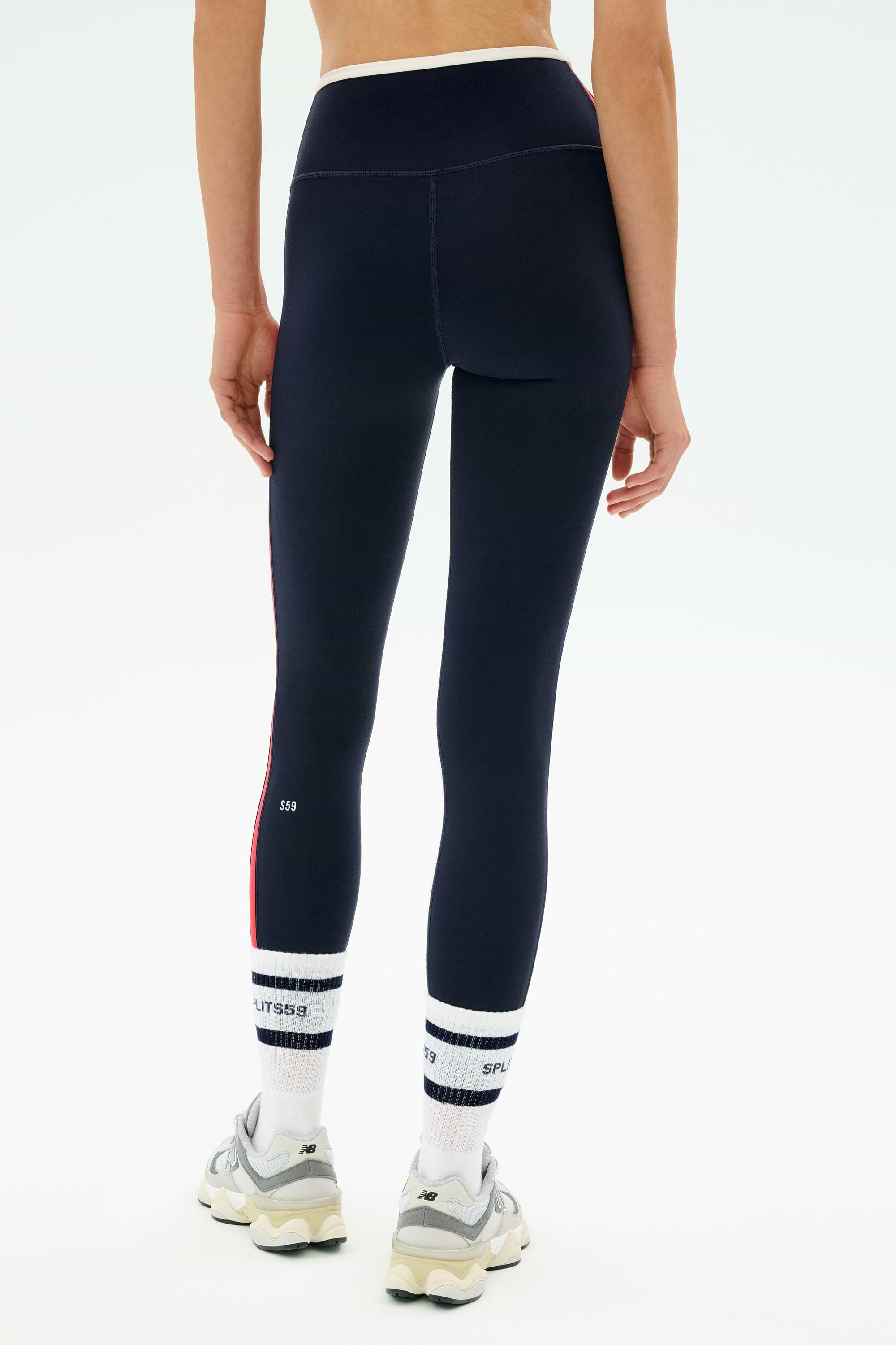 Person wearing SPLITS59 Sam High Waist Rigor 7/8 leggings in Indigo/White, with white and navy socks and beige sneakers, viewed from behind against a plain white background.