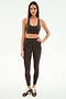 A woman stands facing forward in SPLITS59’s Airweight High Waist Legging in Dark Chocolate with a matching sports bra and black-and-white sneakers, set against a plain white background.
