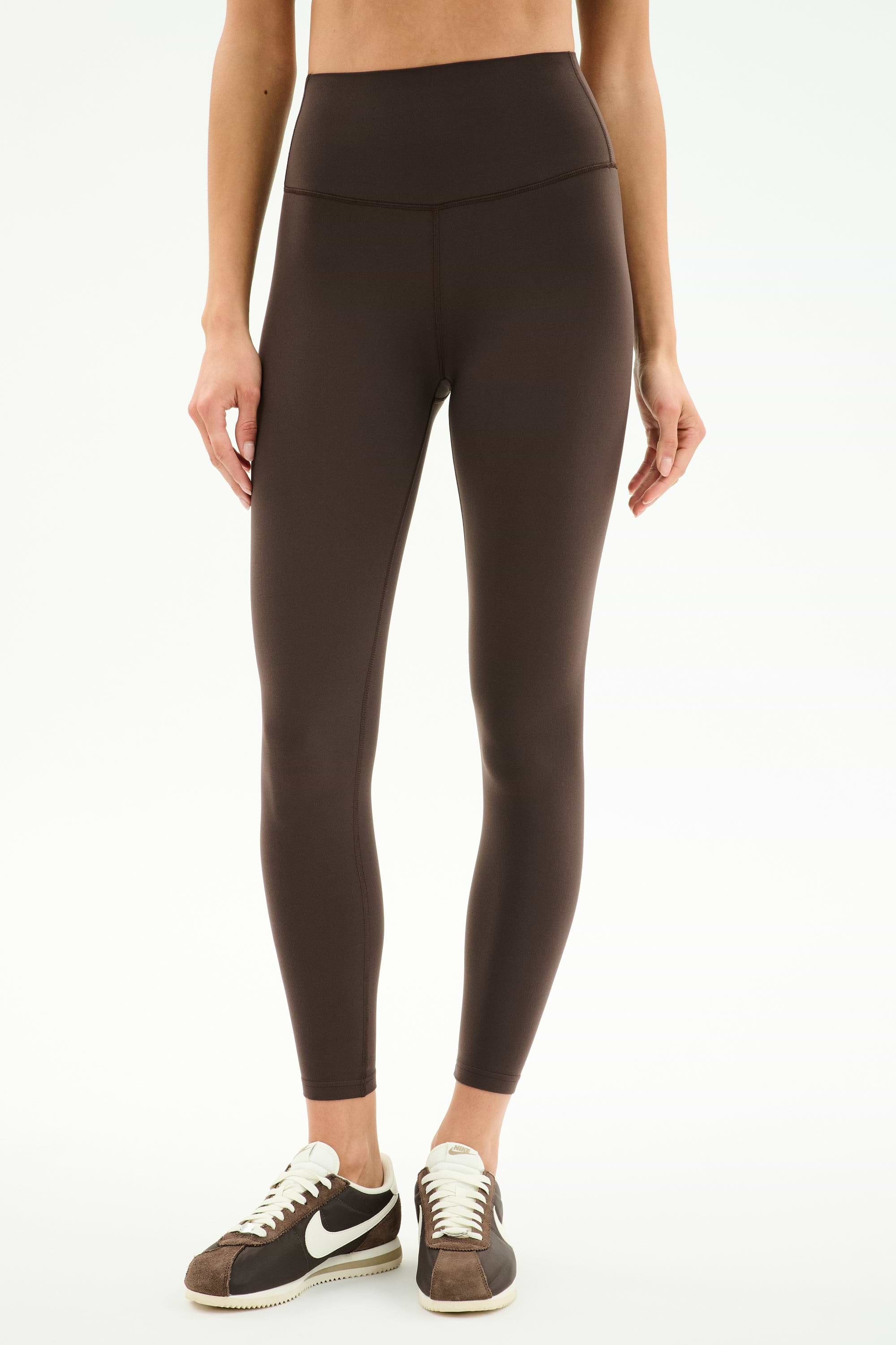 Someone wears SPLITS59's Airweight High Waist Legging in Dark Chocolate and black-and-white sneakers, standing against a plain white background—ideal for hot yoga.