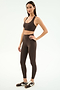 A woman stands in a studio against a white background wearing SPLITS59's Airweight High Waist Legging in Dark Chocolate with a matching brown sports bra and brown Nike sneakers—ideal for hot yoga.