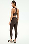 A woman in SPLITS59 Airweight High Waist Legging - Dark Chocolate and a matching sports bra, paired with black and white sneakers, stands sideways against a plain white background.