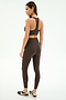 A woman in SPLITS59 Airweight High Waist Legging - Dark Chocolate and a matching sports bra, paired with black and white sneakers, stands sideways against a plain white background.