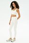 A woman stands against a plain white background wearing the SPLITS59 Airweight Rib High Waist 7/8 leggings in white, paired with a matching crop top and white sneakers with yellow accents.