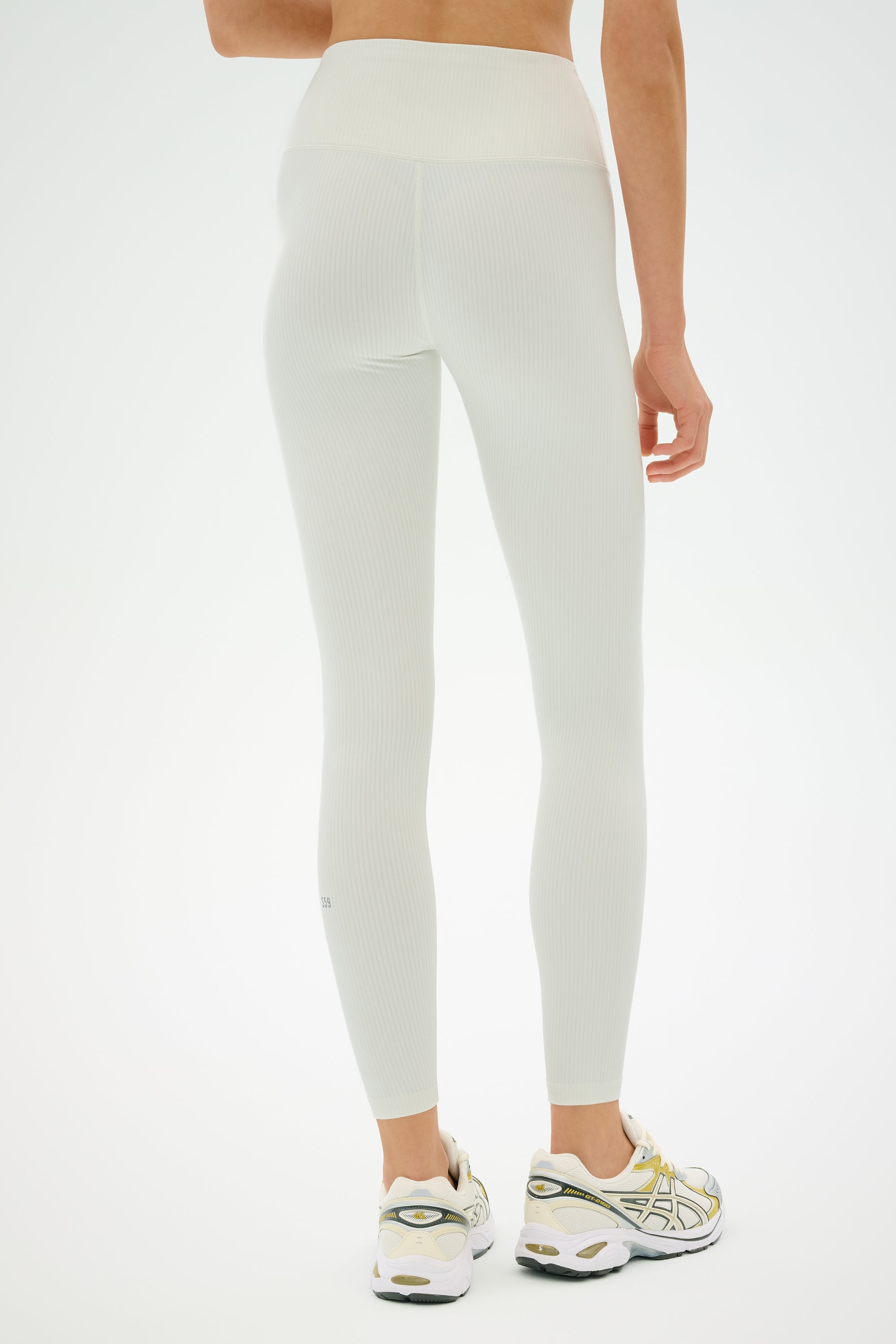 Model wears the SPLITS59 Airweight Rib High Waist 7/8 leggings in white with white athletic shoes, standing on a white background, shown from the back.