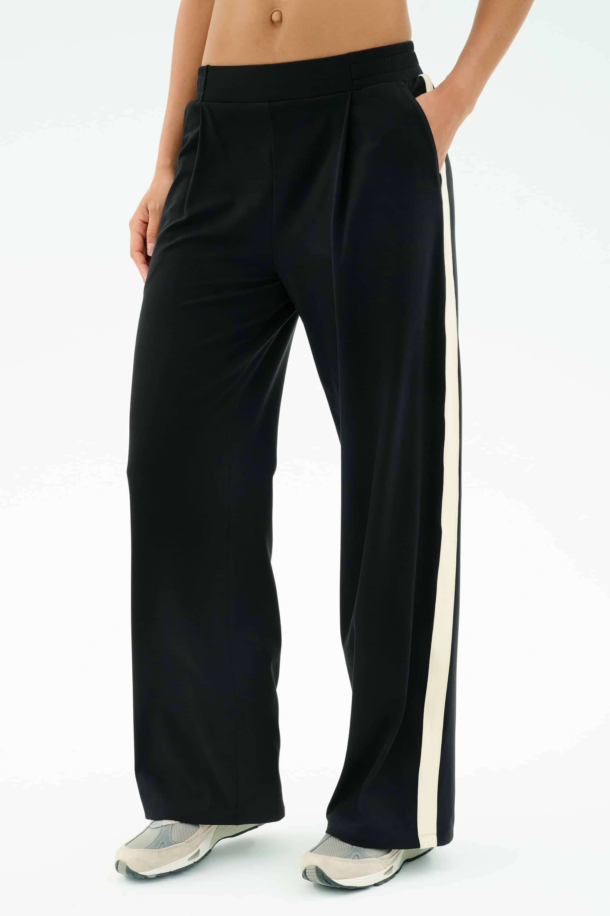 A person wears the SPLITS59 Luca Airweight Trouser with Stripe - Black/White, hands in pockets and paired with white athletic shoes. Made from ultra-luxe Airweight fabric for exceptional comfort and style.
