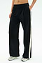 A person wears the SPLITS59 Luca Airweight Trouser with Stripe - Black/White, hands in pockets and paired with white athletic shoes. Made from ultra-luxe Airweight fabric for exceptional comfort and style.