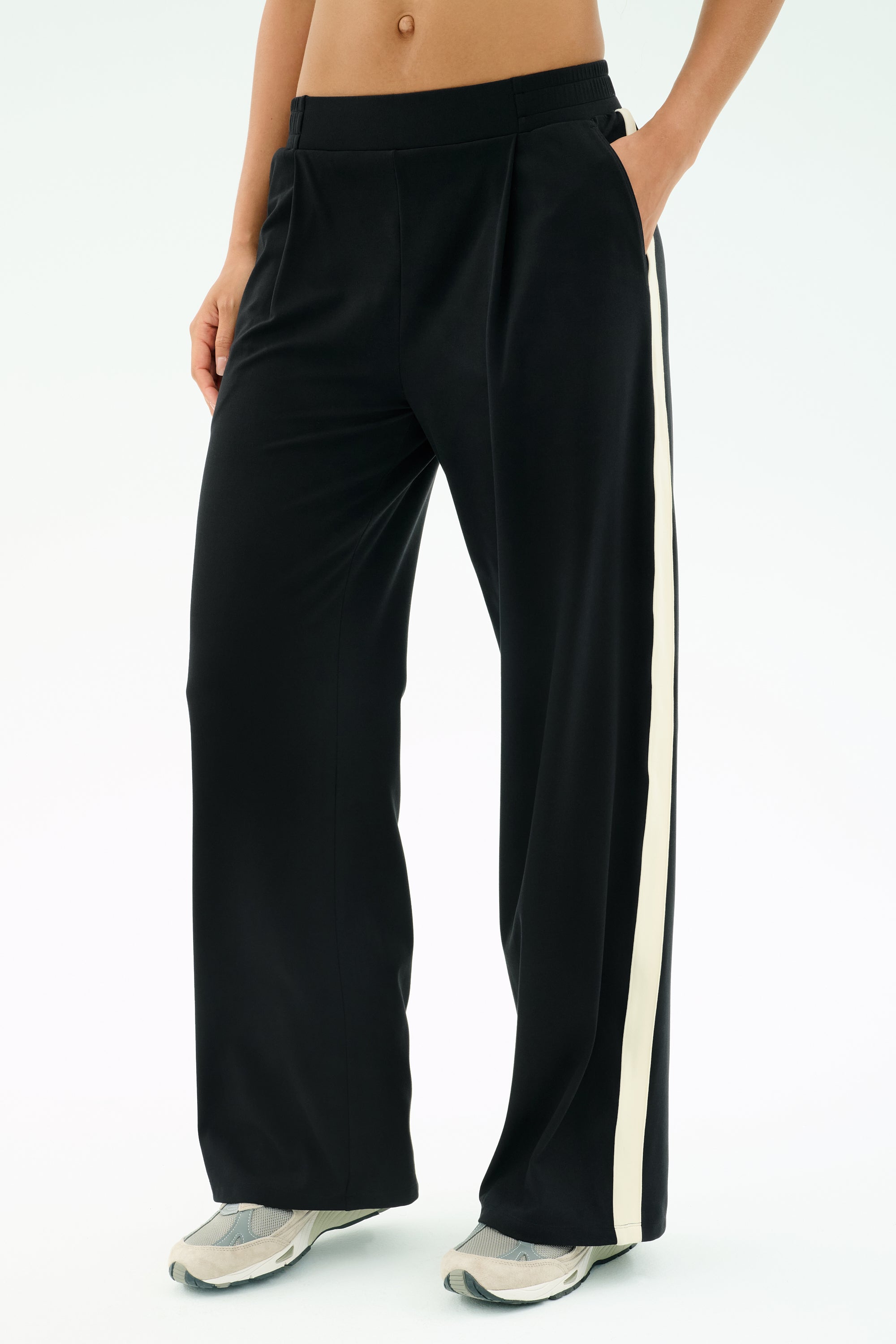 A person wears the SPLITS59 Luca Airweight Trouser with Stripe - Black/White, hands in pockets and paired with white athletic shoes. Made from ultra-luxe Airweight fabric for exceptional comfort and style.