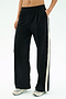 A person wears the SPLITS59 Luca Airweight Trouser with Stripe - Black/White, hands in pockets and paired with white athletic shoes. Made from ultra-luxe Airweight fabric for exceptional comfort and style.