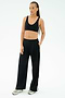 A woman poses against a plain background wearing the SPLITS59 Airweight Scoop Back Bra in black, paired with black wide-leg pants and sneakers, one hand in her pocket.