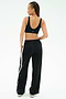 A person is seen from behind against a white background wearing the SPLITS59 Airweight Scoop Back Bra in black and wide-leg pants with a white side stripe.