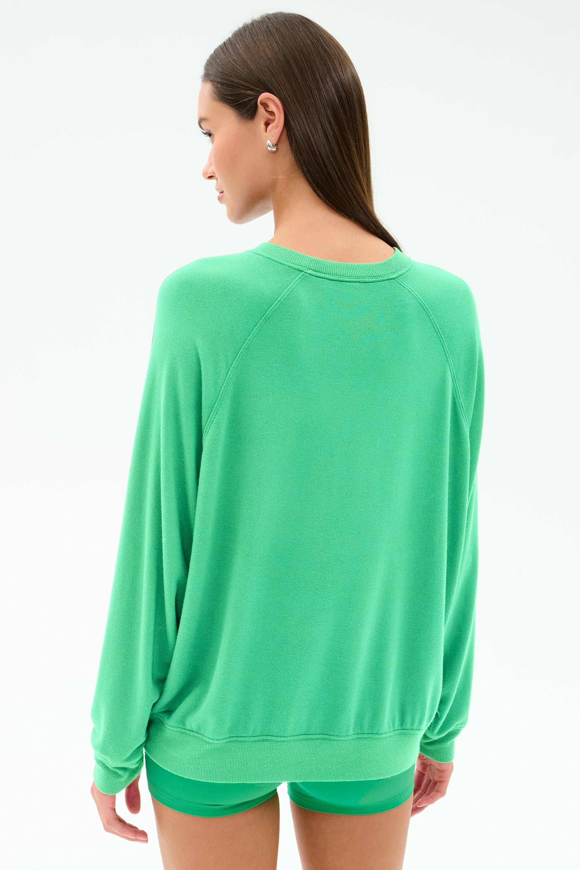 A woman with straight brown hair wears the SPLITS59 Andie Oversized Fleece Sweatshirt in Spearmint, paired with matching shorts, as she stands facing away from the camera against a plain white background.