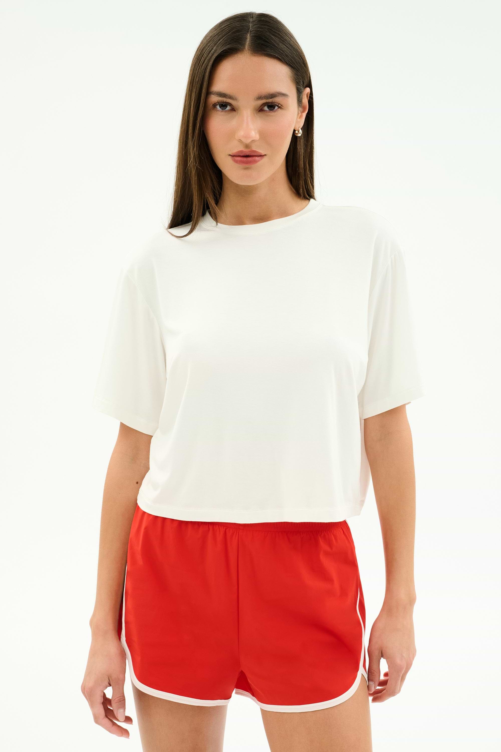 A person faces forward against a white background, wearing the SPLITS59 Djuna Oversized Jersey Tee in white and red athletic shorts with white trim.