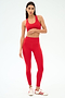 A woman stands against a light background wearing the SPLITS59 Sara Airweight Bra in Pirate Red with matching leggings and white sneakers with red stripes—perfect for Pilates or hot yoga.