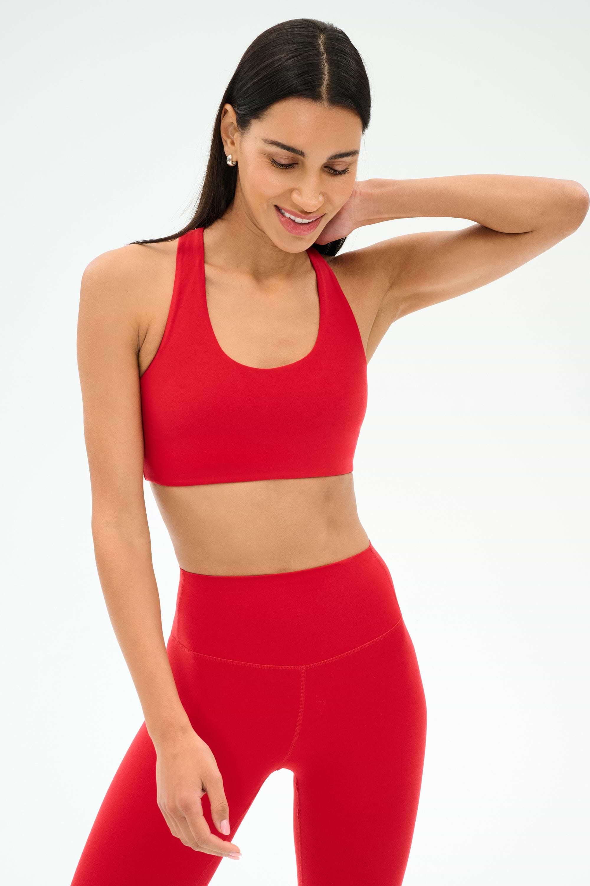 A woman wears the SPLITS59 Sara Airweight Bra in Pirate Red with matching high-waisted leggings, posing against a plain light background—ideal for hot yoga or Pilates.
