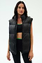A woman wears the SPLITS59 Summit Nylon Puffer Vest in black over a sports bra and leggings, standing against a plain light background—the perfect lightweight layer for cool weather workouts.