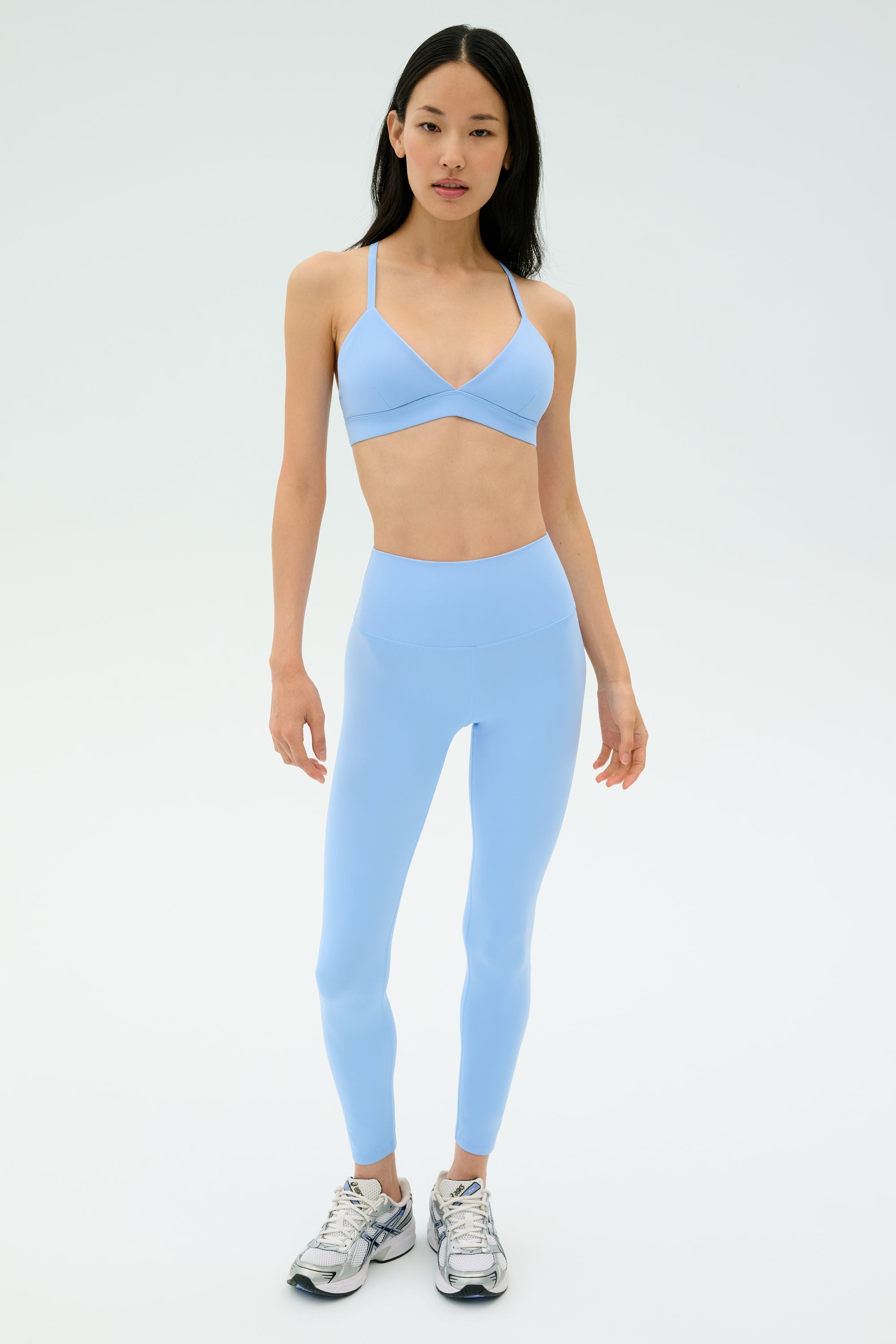 A woman faces forward wearing the SPLITS59 Theo Rigor Bra in Skylight with matching leggings and silver athletic shoes, set against a plain light background.