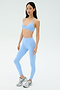 A person wears the SPLITS59 Theo Rigor Bra in Skylight, styled with matching high-waisted leggings and white athletic shoes against a plain light background.