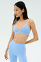 A woman wears the SPLITS59 Theo Rigor Bra in Skylight, paired with matching high-waisted leggings, standing against a plain background.