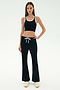 A woman stands facing forward against a plain white background, wearing SPLITS59's Blaire Rib Pant in black paired with a black crop top with white trim and white sneakers.