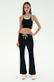 A woman stands facing forward against a plain white background, wearing SPLITS59's Blaire Rib Pant in black paired with a black crop top with white trim and white sneakers.